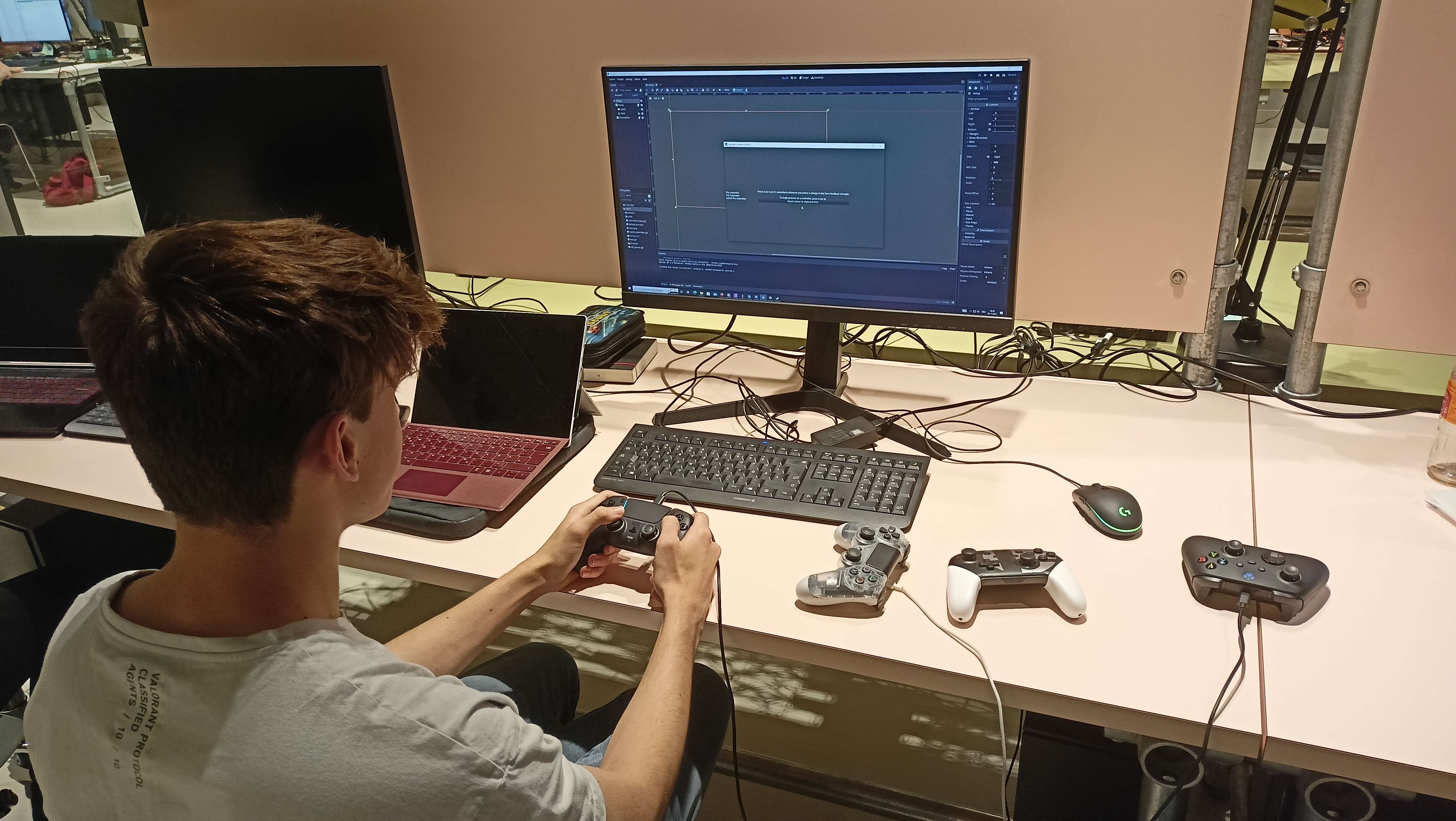 **Figure 13:** Photo of a typical test situation: A human is sitting in front of a computer, Godot with some UI is visible on the monitor, different controllers are on the table and one is being tested with.